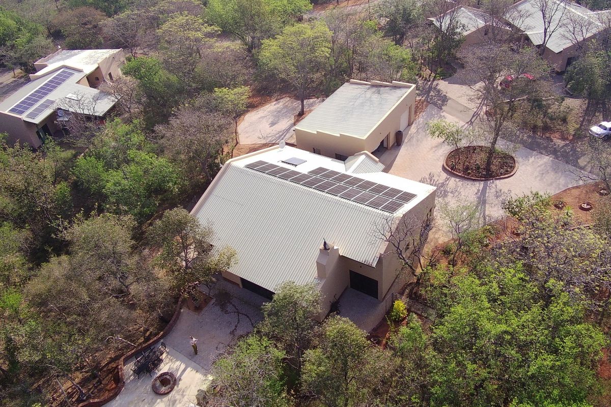 Aerial view of a residential property featuring a main house with solar panels, a detached garage, and a paved driveway set in a wooded area.