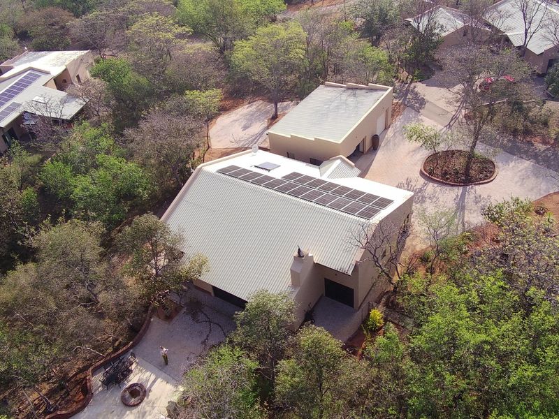 Aerial view of a residential property featuring a main house with solar panels, a detached garage, and a paved driveway set in a wooded area.