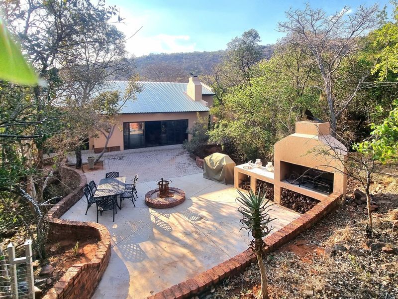 Outdoor patio area featuring a built-in braai, concrete flooring, and brick retaining walls, set within a natural bushveld environment.