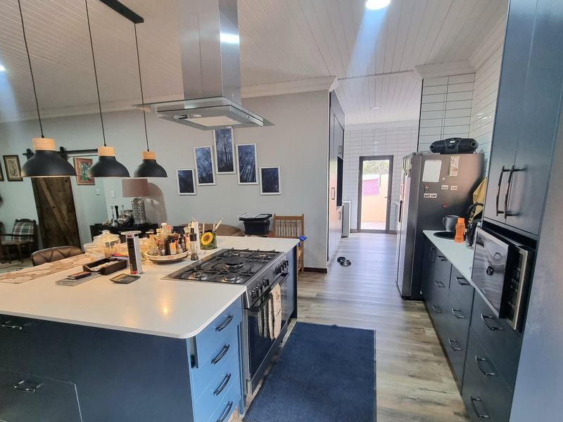 Modern open-plan kitchen featuring a central island with gas cooktop, dark cabinetry, subway tile backsplash, and integrated appliances, flowing into the living area.