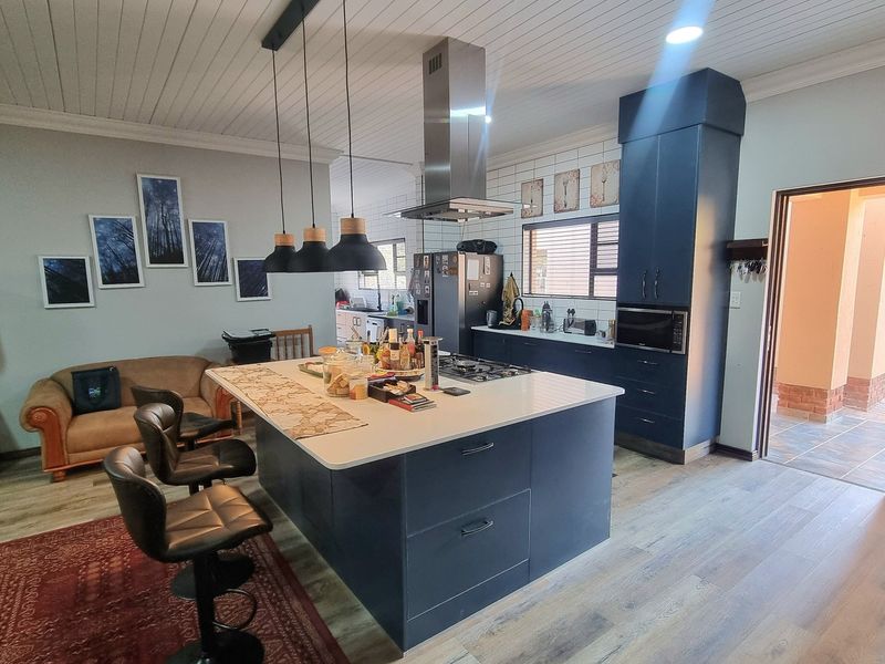 Modern open-plan kitchen featuring a large central island, dark cabinetry, stainless steel extractor fan, and high-quality laminate flooring.