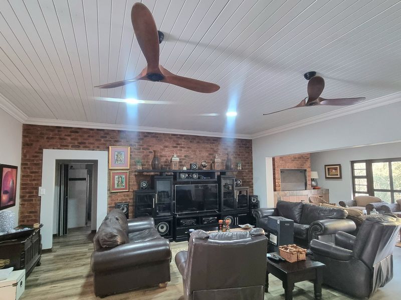Spacious living room featuring an exposed brick feature wall, timber-look flooring, and a tongue and groove ceiling with integrated ceiling fans.