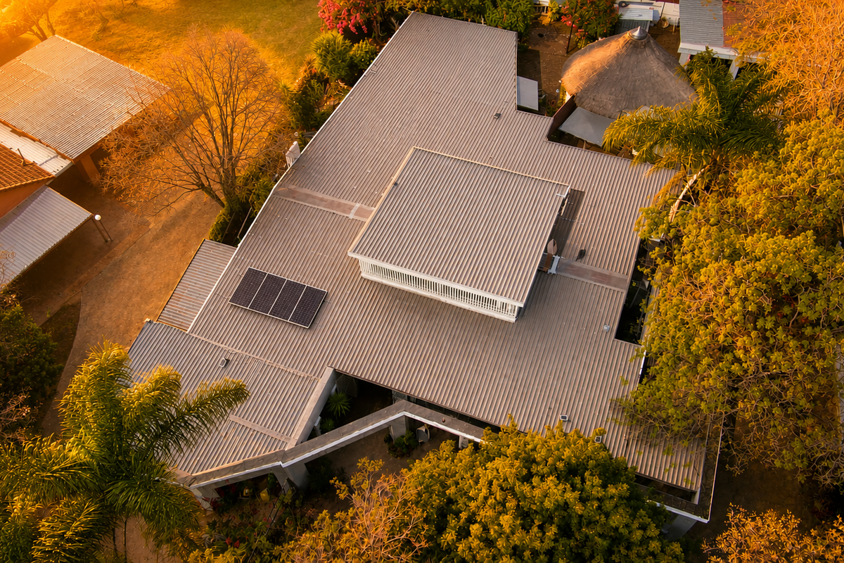 Aerial view of the property showcasing the corrugated metal roof, integrated solar panels, surrounding garden, and a detached thatch roof gazebo.