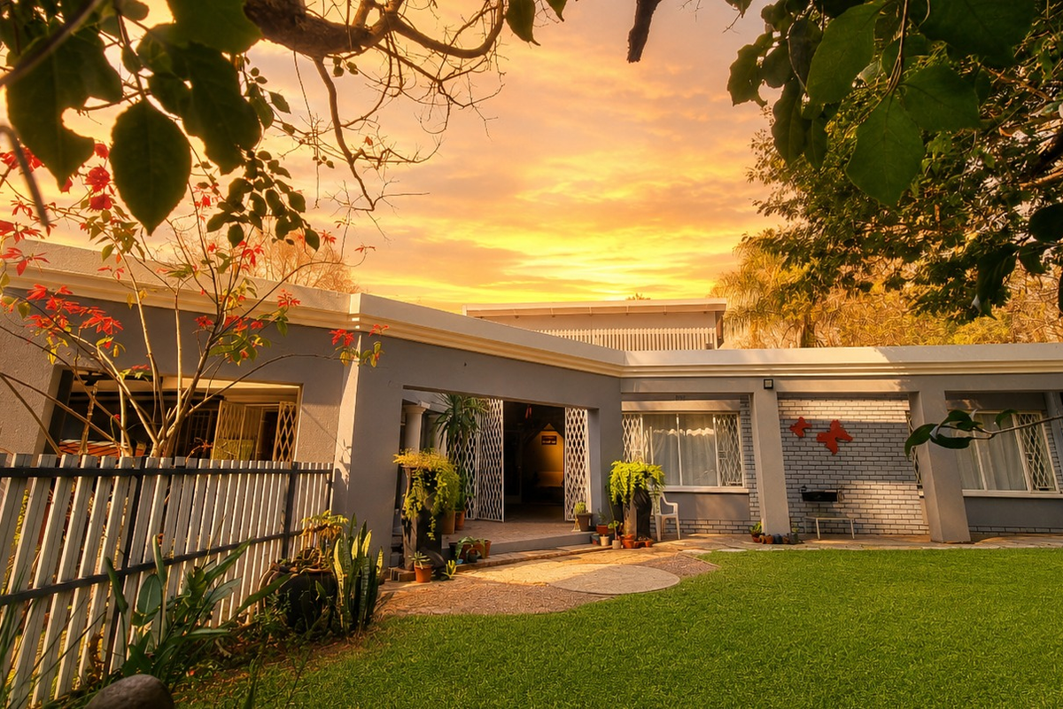 A well-maintained rear exterior view of the house featuring a paved patio, manicured lawn, and secure access points under a vibrant sunset sky.