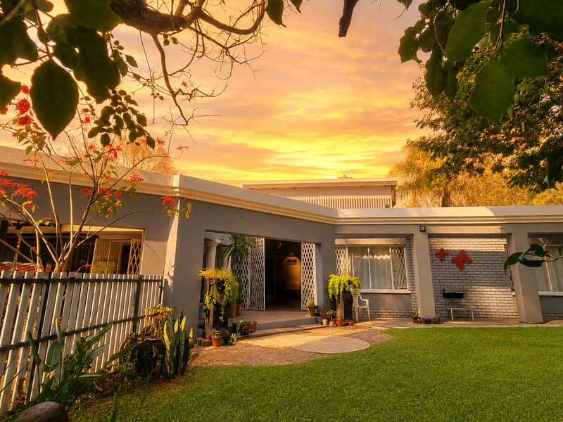 A well-maintained rear exterior view of the house featuring a paved patio, manicured lawn, and secure access points under a vibrant sunset sky.