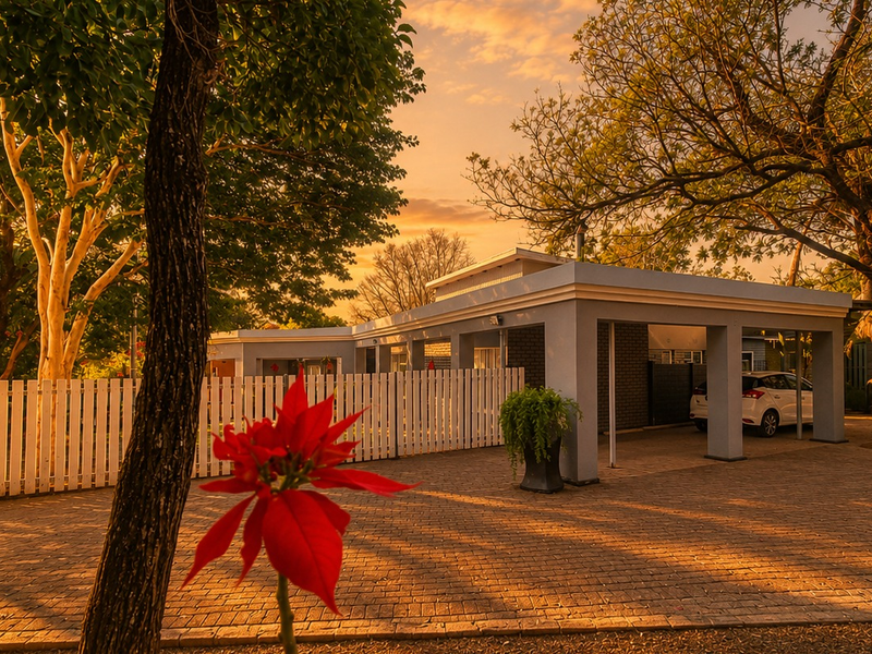 A well-maintained front exterior view featuring a paved driveway, covered carport, and classic white picket fencing set against a beautiful sunset backdrop.