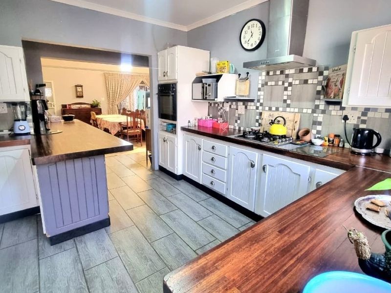 A functional kitchen featuring white cabinetry, wooden countertops, a gas hob with extractor fan, and tiled flooring, with an open-plan flow to the dining area.
