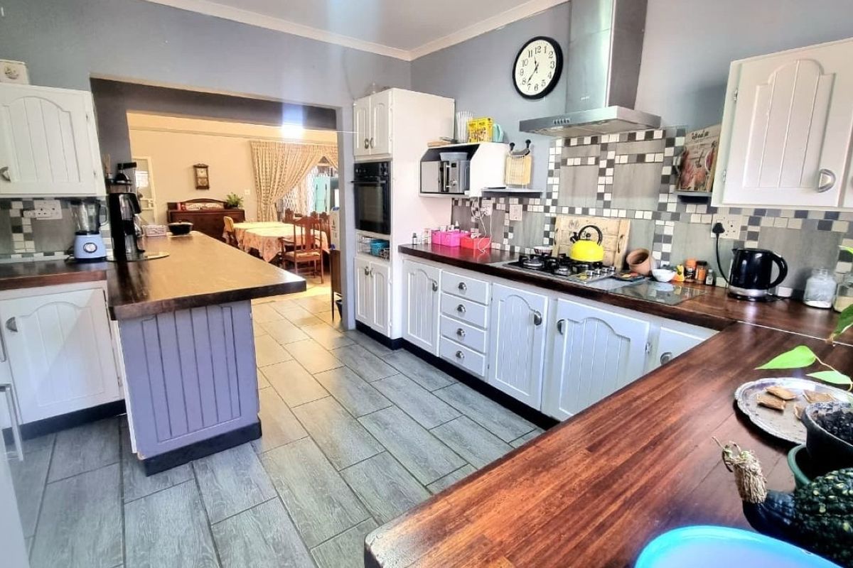 A functional kitchen featuring white cabinetry, wooden countertops, a gas hob with extractor fan, and tiled flooring, with an open-plan flow to the dining area.