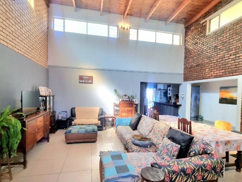 Spacious open-plan living and dining area featuring high vaulted ceilings with exposed timber beams, exposed brick walls, and abundant natural light from clerestory windows.