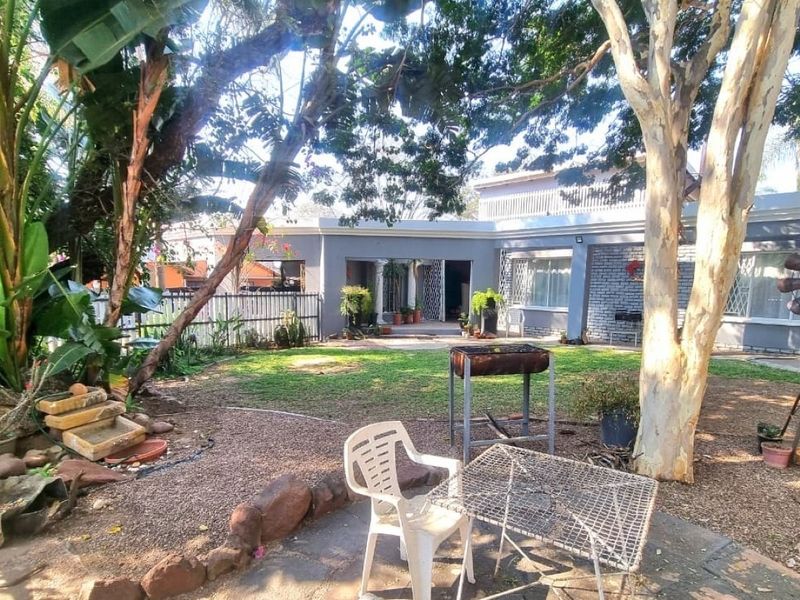 A spacious rear garden featuring a lawn, mature trees, and a brick-finished house exterior with a paved patio area.