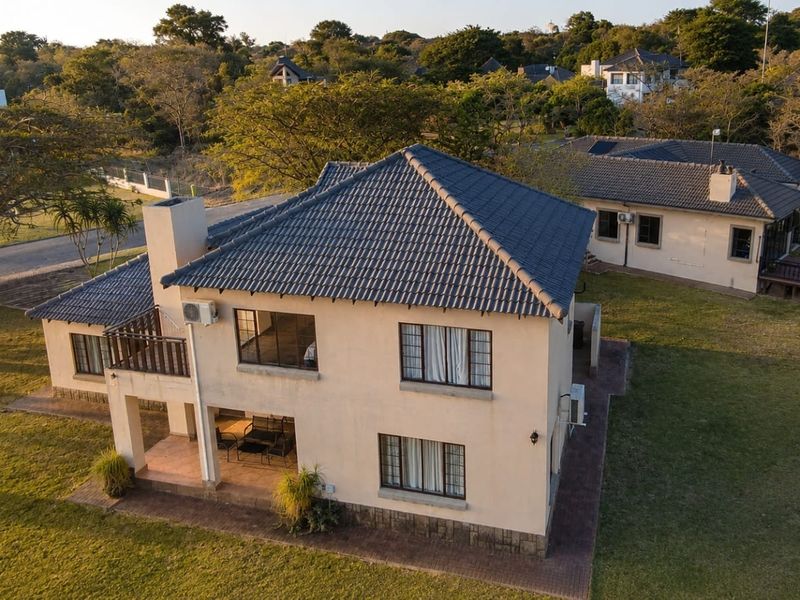 Aerial view of a two-story residential house featuring a tiled roof, chimney, balcony, and a paved patio area set within a landscaped garden.