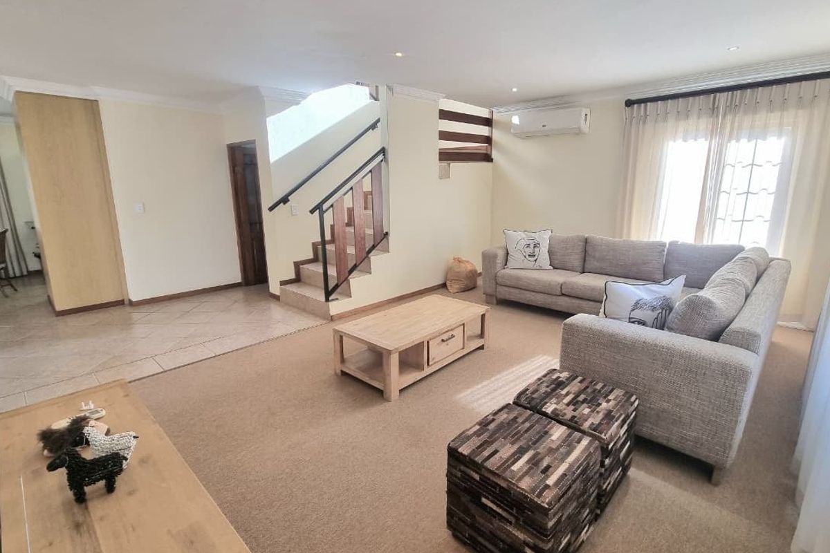 Spacious living room featuring a central staircase, split-system air conditioning, and a combination of tiled and carpeted flooring with neutral wall finishes.