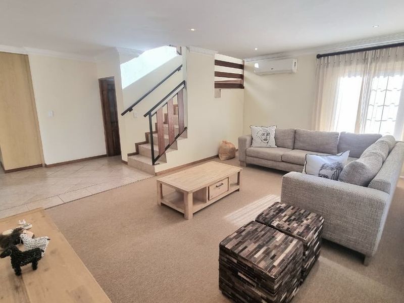 Spacious living room featuring a central staircase, split-system air conditioning, and a combination of tiled and carpeted flooring with neutral wall finishes.