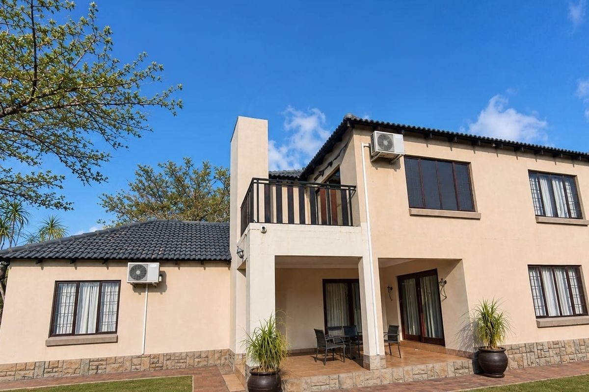 Rear view of a two-story residential property featuring a covered patio, upper balcony, tiled roof, and stone cladding accents.
