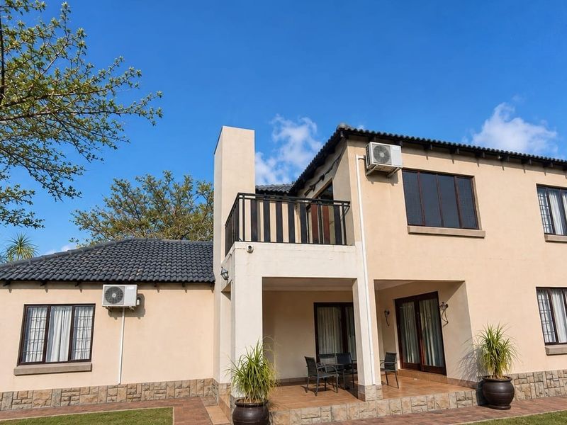 Rear view of a two-story residential property featuring a covered patio, upper balcony, tiled roof, and stone cladding accents.