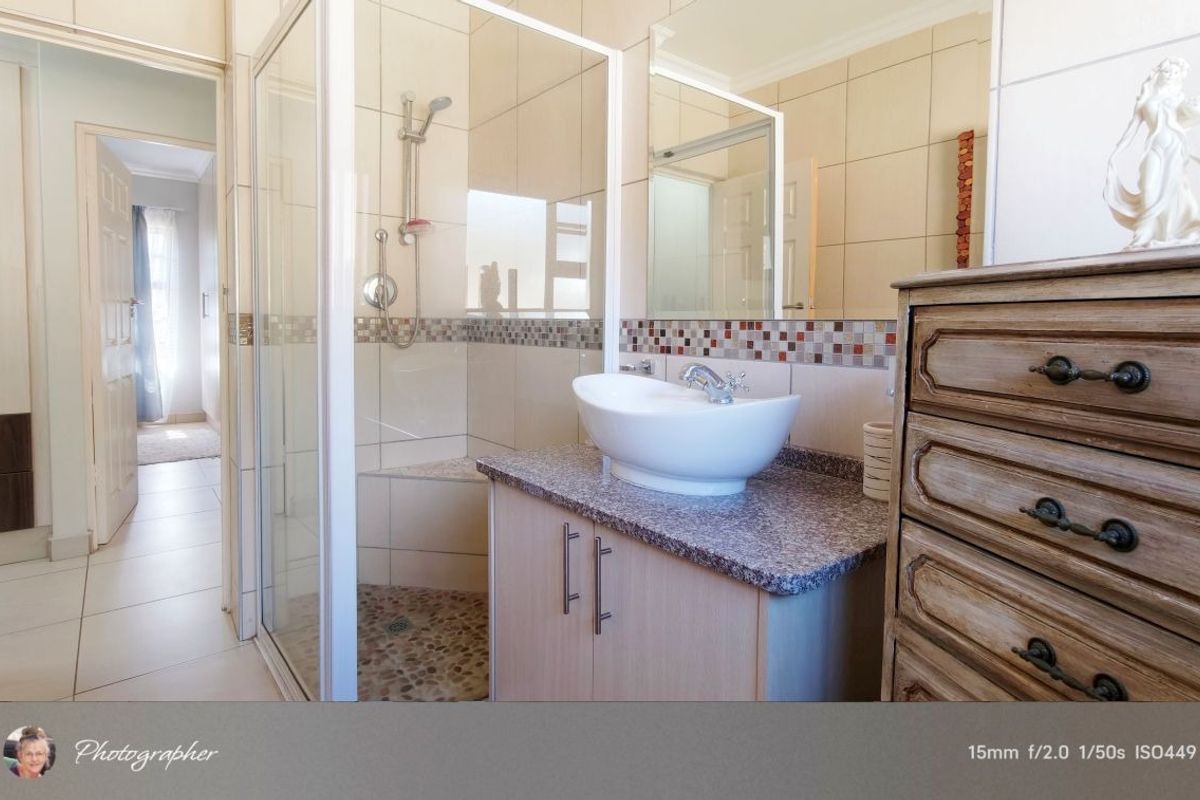 A well-maintained bathroom featuring a glass-enclosed shower with pebble flooring, a modern vessel sink on a granite vanity, and decorative mosaic tile accents.