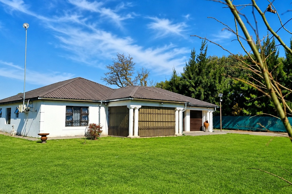 A view of the rear exterior of the house featuring a tiled roof, covered patio area with columns, and a spacious lawn.