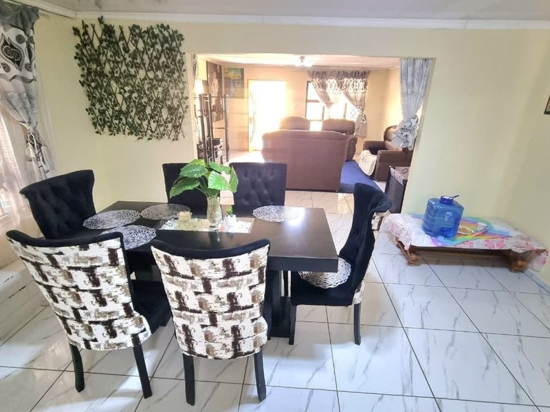 Open plan living and dining area featuring light-colored tiled flooring and coved ceilings, providing a connected layout between the two living spaces.