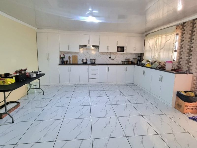 Spacious kitchen featuring white cabinetry, marble-look floor tiles, built-in appliances, and a modern drop ceiling, offering a clean and functional layout.
