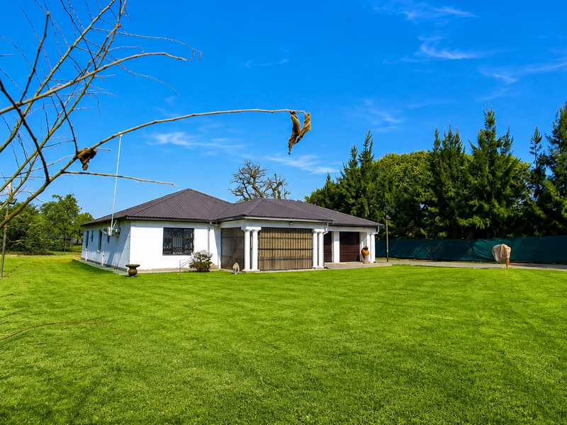 A well-maintained single-story house featuring a spacious lawn, covered patio with columns, and an integrated double garage under a dark tiled roof.