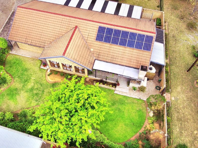 Aerial view of a residential property featuring a tiled roof with integrated solar panels, a paved patio area, and a well-maintained garden.