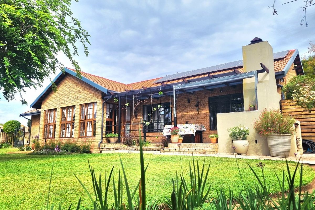 Rear view of a brick house featuring a paved patio, pergola, outdoor fireplace, and solar panels set within a well-maintained garden.