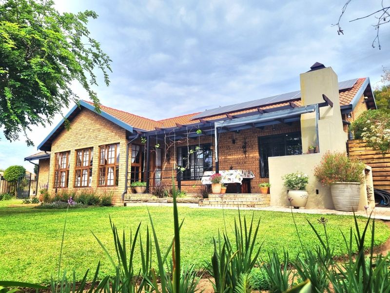 Rear view of a brick house featuring a paved patio, pergola, outdoor fireplace, and solar panels set within a well-maintained garden.