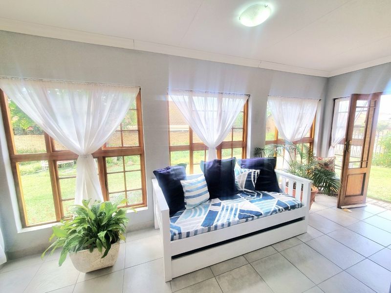 A bright, enclosed patio area featuring tiled flooring, large timber-framed windows, and direct access to the garden.