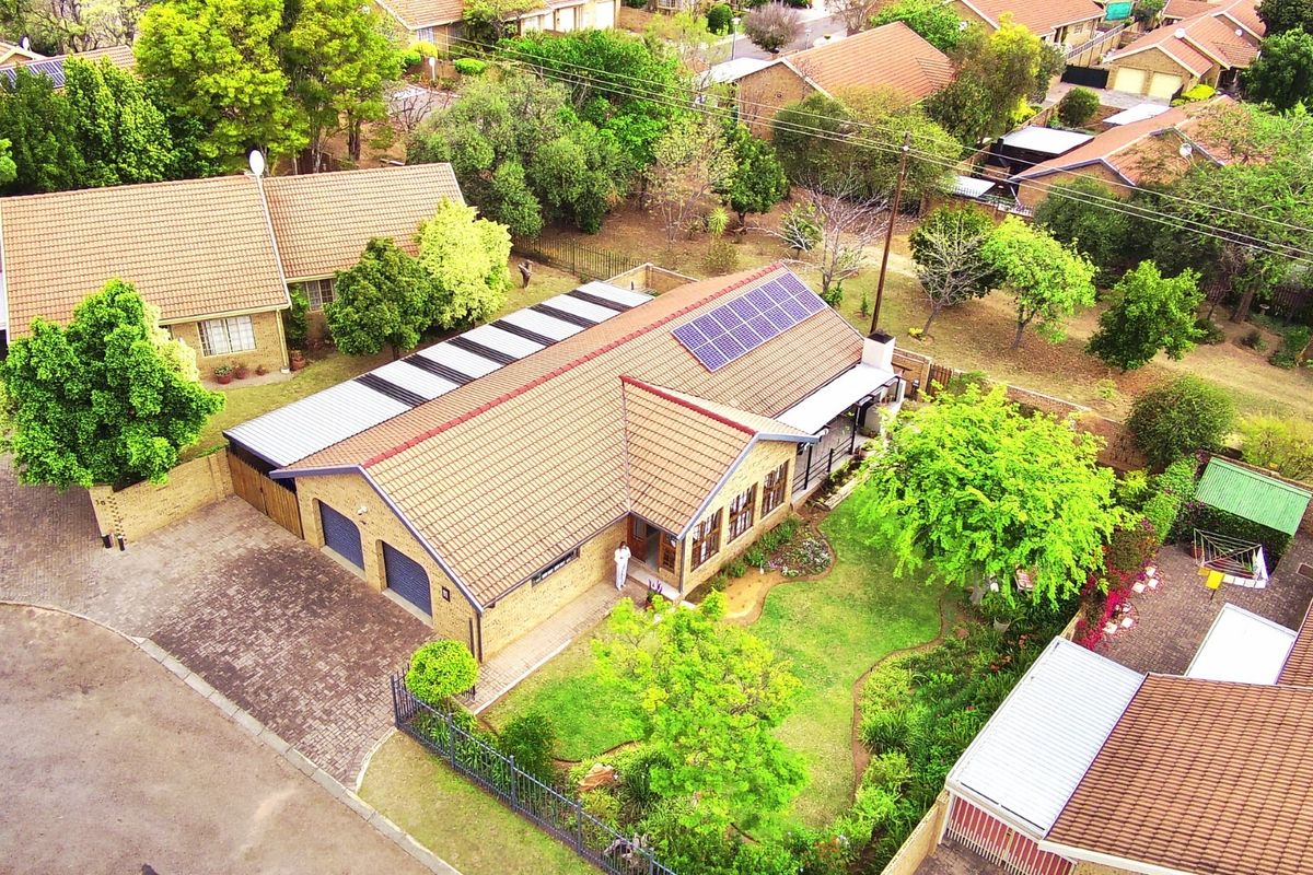 Aerial view of a residential property featuring a tiled roof with solar panels, a double garage, paved driveway, and a well-maintained garden.