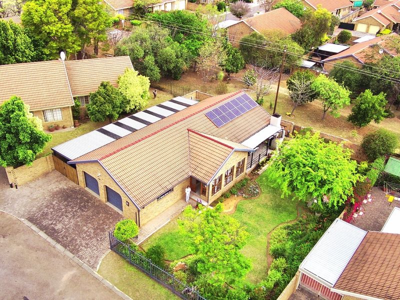 Aerial view of a residential property featuring a tiled roof with solar panels, a double garage, paved driveway, and a well-maintained garden.