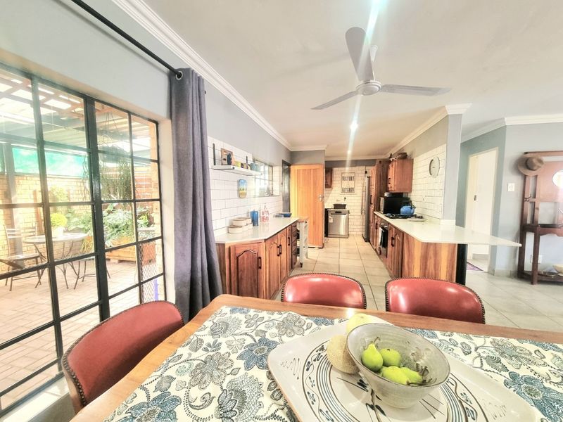 Open-plan kitchen and dining area featuring wooden cabinetry, subway tile backsplash, stone countertops, and direct access to an outdoor patio through sliding glass doors.