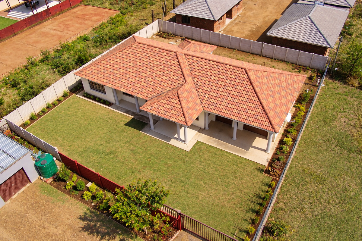 Aerial view of a residential property featuring a tiled roof house, a spacious lawn, a detached garage, and a secure perimeter wall.