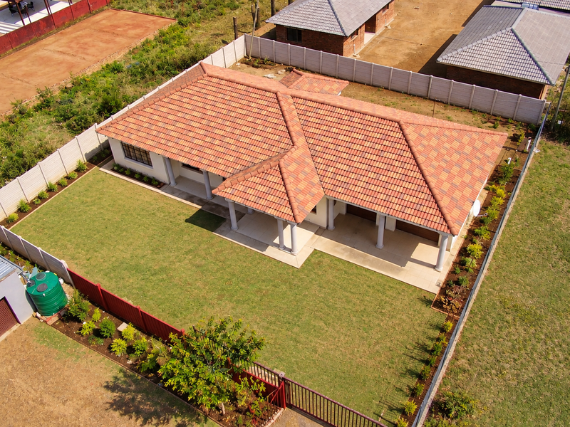 Aerial view of a residential property featuring a tiled roof house, a spacious lawn, a detached garage, and a secure perimeter wall.
