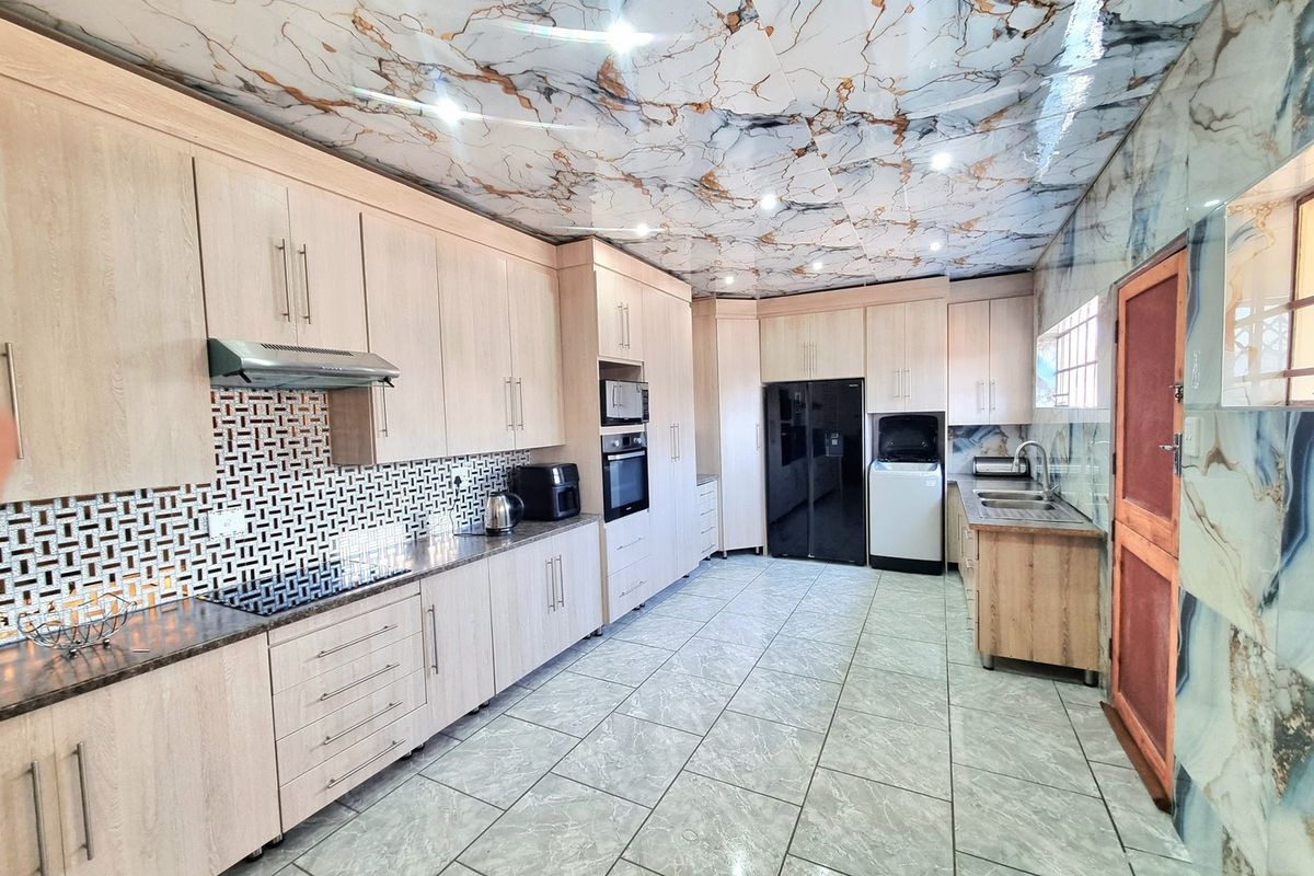 Spacious kitchen featuring light wood cabinetry, built-in appliances, a double sink, and distinctive marble-effect ceiling and wall finishes.