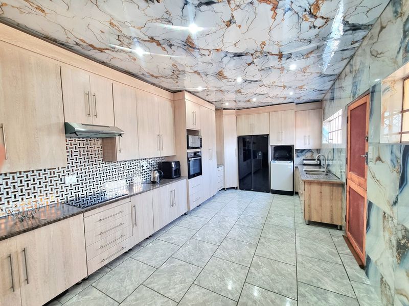 Spacious kitchen featuring light wood cabinetry, built-in appliances, a double sink, and distinctive marble-effect ceiling and wall finishes.