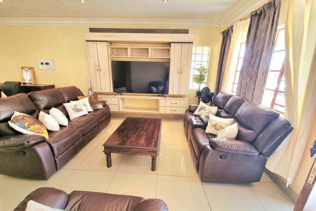 A spacious living room featuring large format floor tiles, recessed ceiling lighting, and a custom built-in media wall unit.