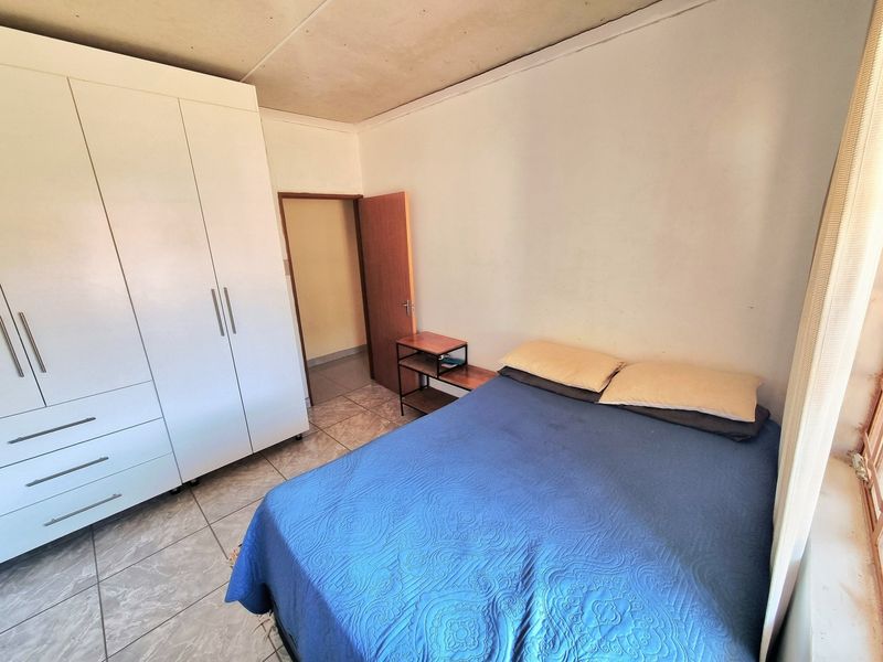 A bedroom featuring tiled flooring and a built-in wardrobe, showing signs of ceiling wear and requiring cosmetic updates.