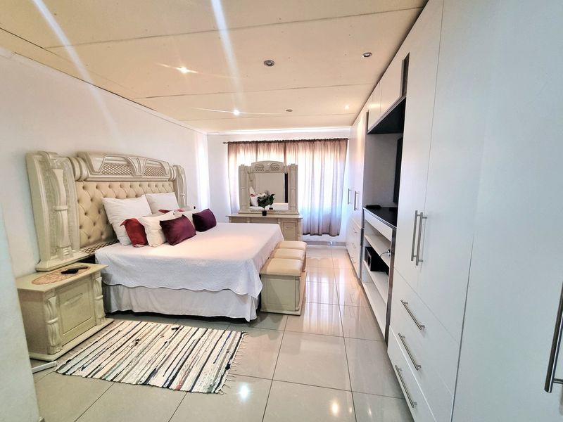 Spacious bedroom featuring large built-in cupboards, polished tiled flooring, and recessed downlighting, offering a clean and functional living space.