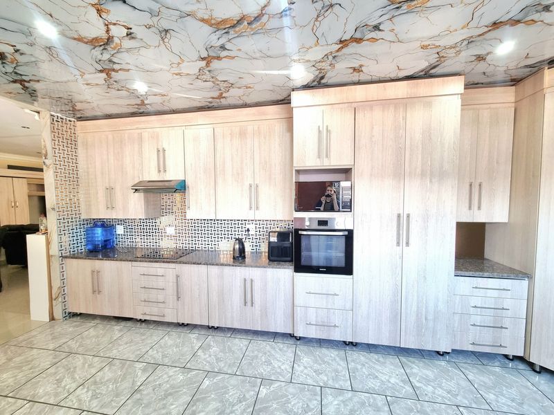 Modern kitchen featuring light wood-grain cabinetry, granite countertops, built-in appliances, mosaic backsplash, and a distinctive marble-effect ceiling finish.