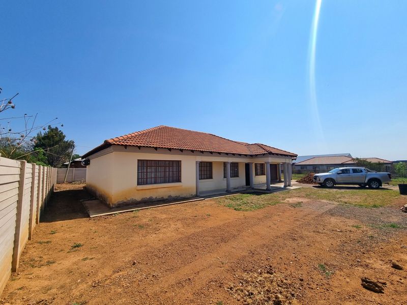 Front exterior view of a single-story house featuring a tiled roof, concrete columns, and a large unlandscaped yard with a boundary wall.