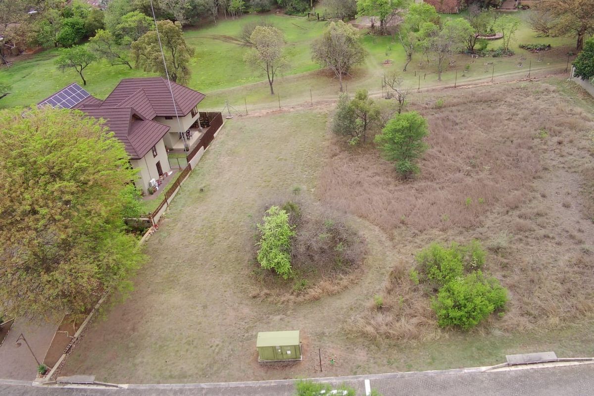 An aerial view of a vacant residential plot featuring natural vegetation, perimeter fencing, and an adjacent residential property.