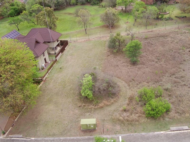 An aerial view of a vacant residential plot featuring natural vegetation, perimeter fencing, and an adjacent residential property.
