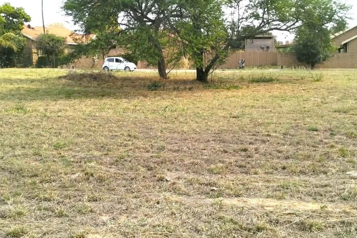 A view of a vacant residential plot featuring natural grassland and mature trees, situated in a developed suburban neighborhood.