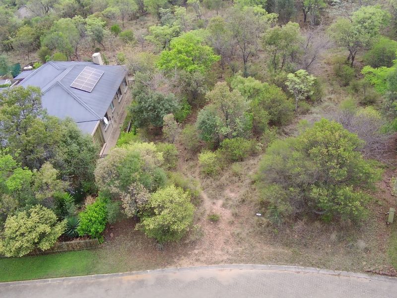 Aerial view of a residential vacant land plot featuring established trees, natural vegetation, and adjacent property infrastructure.