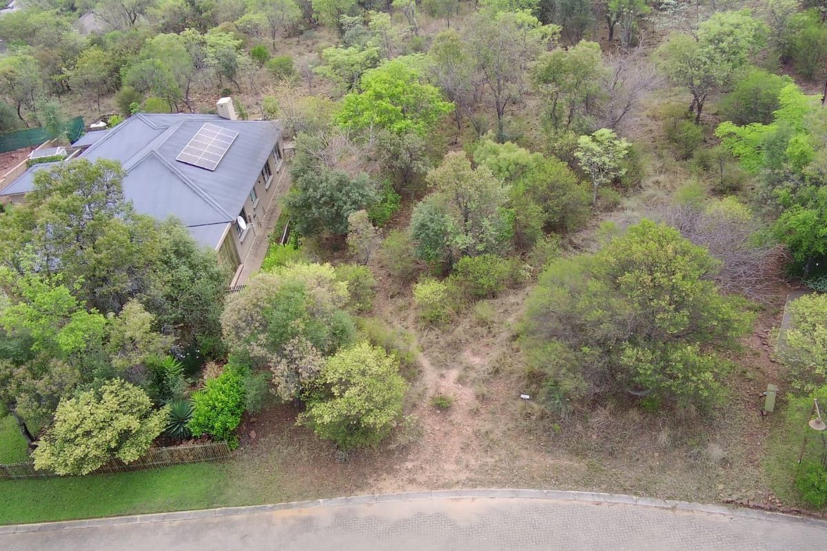 Aerial view of a residential vacant land plot featuring established trees, natural vegetation, and adjacent property infrastructure.