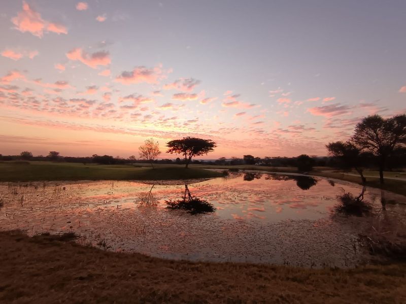 A scenic view of a natural pond and surrounding landscape at sunset, showcasing the tranquil outdoor environment of the vacant land property.