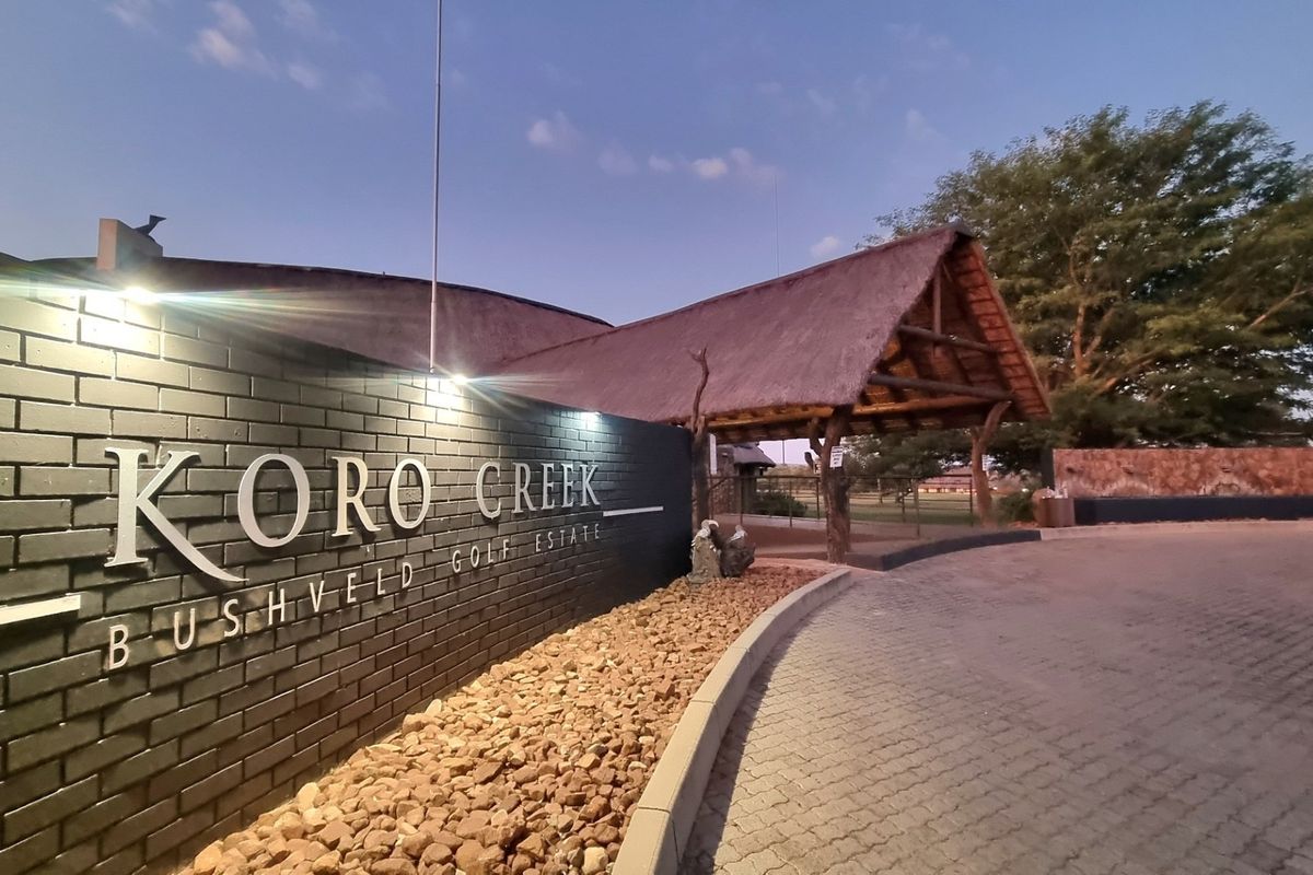 Entrance view of Koro Creek Bushveld Golf Estate featuring a brick boundary wall, paved driveway, and a thatched roof structure.