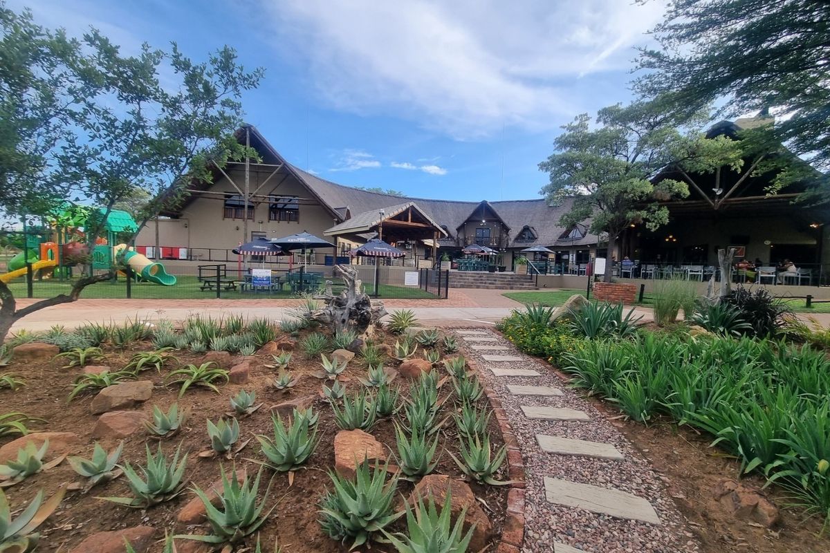 A well-maintained clubhouse facility featuring a thatched roof, expansive outdoor seating areas, and beautifully landscaped gardens with a stone-paved pathway.