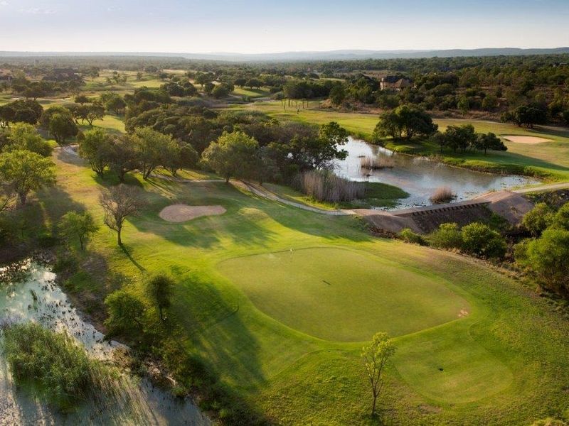 An aerial view of a well-maintained golf course featuring lush green fairways, putting greens, and natural water hazards within a scenic landscape.