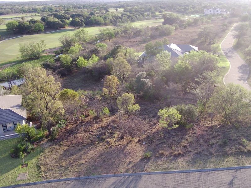 Aerial view of a vacant residential plot featuring established trees and proximity to a golf course, situated within a developed estate.